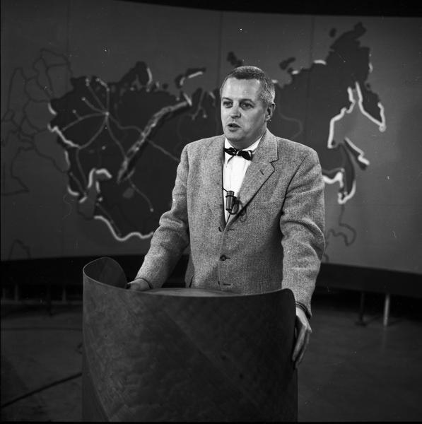 Robert Byrnes on television set, standing at lectern